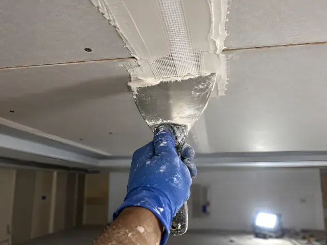 Joint compound being applied over fibre-mesh tape along a gypsum ceiling seam.